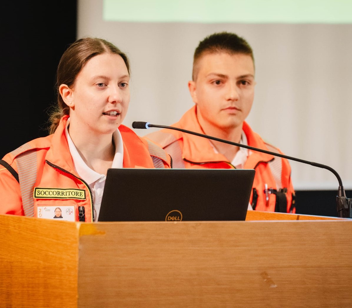 Relatrice sul palco che parla durante il meeting dei giovani. Al suo fianco un ragazzo volontario